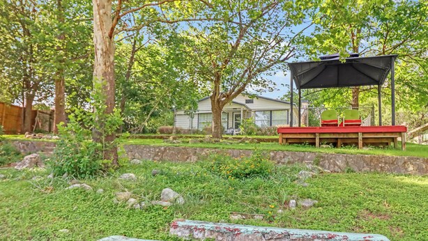 Patio trasero con zona de estar cubierta, un muro de piedra y una casa al fondo.