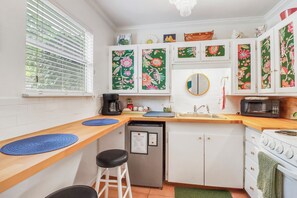 A compact kitchen with white cabinets, a coffee maker, a microwave, and a stove. - Darling cottage on the Blanco River. Minutes from downtown Wimberley! (Wimberley)