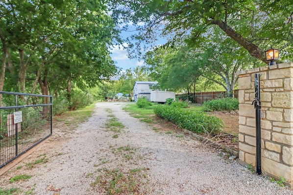 A gravel driveway leading to a gated area with a house and a trailer in the background.
