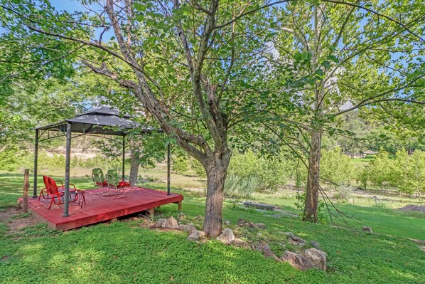 A gazebo with a table and chairs in a grassy area with trees.
