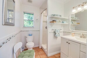 A bathroom with a toilet, shower, and sink. There is a window and a mirror above the sink. - Darling cottage on the Blanco River. Minutes from downtown Wimberley! (Wimberley)