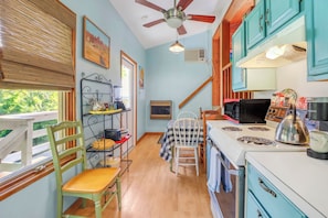 A kitchen with a stove, microwave, kettle, and various appliances. There is a window with blinds, a chair, and a table with a checkered tablecloth. - Cozy and clean loft on the Blanco River - Minutes from downtown Wimberley! (Wimberley)