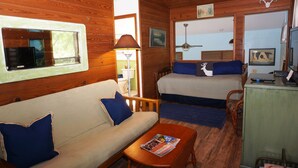 Una cabaña acogedora con interior de madera, un sofá, una cama, un escritorio y un ventilador de techo.