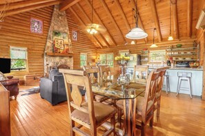 Interior rústico con comedor, cocina y chimenea de piedra.