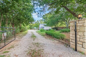 Un camino de grava que conduce a una zona vallada con una casa y un remolque al fondo.