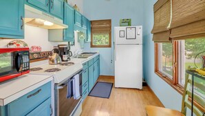 Una cocina compacta con gabinetes color turquesa, una estufa blanca, un microondas rojo y un refrigerador blanco.