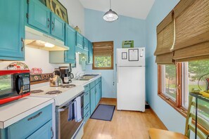 Una cocina compacta con gabinetes color turquesa, una estufa blanca, un microondas rojo y un refrigerador blanco.