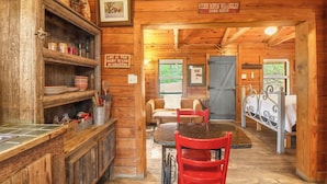 A rustic wooden interior with a dining area, a kitchen with shelves, and a sign that reads 'RIDIN ROPIN WRANGLIN DONE HERE'.