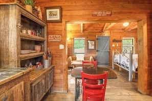 Un intérieur rustique en bois, avec un coin repas, une cuisine dotée d’étagères et une enseigne sur laquelle on peut lire : « C’est ici qu’on fait du rodéo, du lasso et qu’on s’occupe des chevaux ».