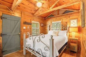 Une chambre à coucher dans une cabane en bois, avec un lit, une fenêtre, une porte et une petite table de chevet avec une lampe.