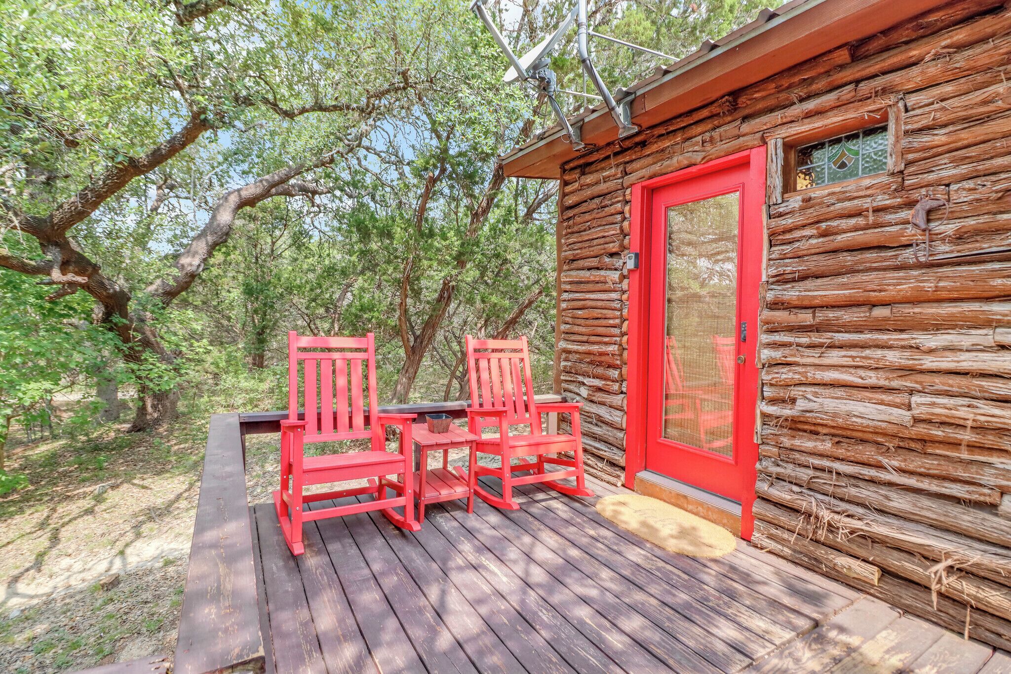 Una cabaña de madera con puerta roja y dos sillas rojas en una terraza de madera.