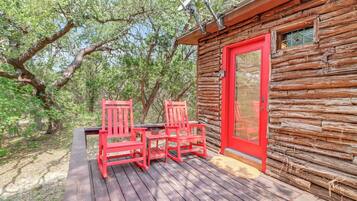 Una cabaña de madera con puerta roja y dos sillas rojas en una terraza de madera.
