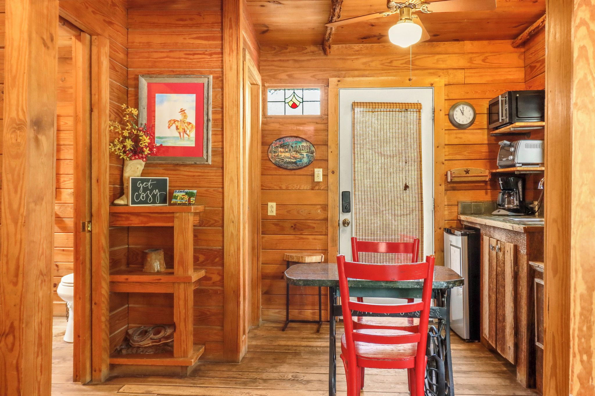 A wooden cabin interior with a dining area, kitchen, and a door leading to another room.