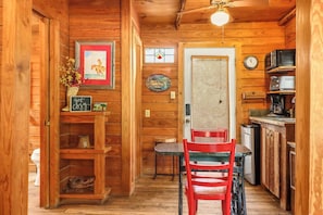 L’intérieur d’une cabane en bois comprend un coin repas, une cuisine et une porte qui donne sur une autre pièce.