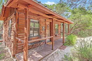 A wooden cabin with a porch, a table, and a chair. - Private, cozy and romantic cabin - a Wimberley favorite! Private hot tub! (Wimberley)