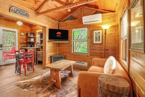 A wooden cabin interior with a dining area, a sofa, a television, and a fireplace. - Private, cozy and romantic cabin - a Wimberley favorite! Private hot tub! (Wimberley)