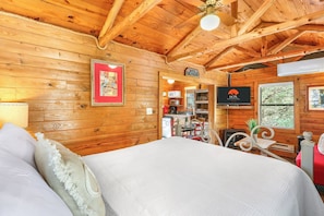 A wooden cabin interior with a bed, a television, and a kitchenette. - Private, cozy and romantic cabin - a Wimberley favorite! Private hot tub! (Wimberley)
