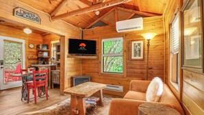 A wooden cabin interior with a dining area, a sofa, a television, and a fireplace.