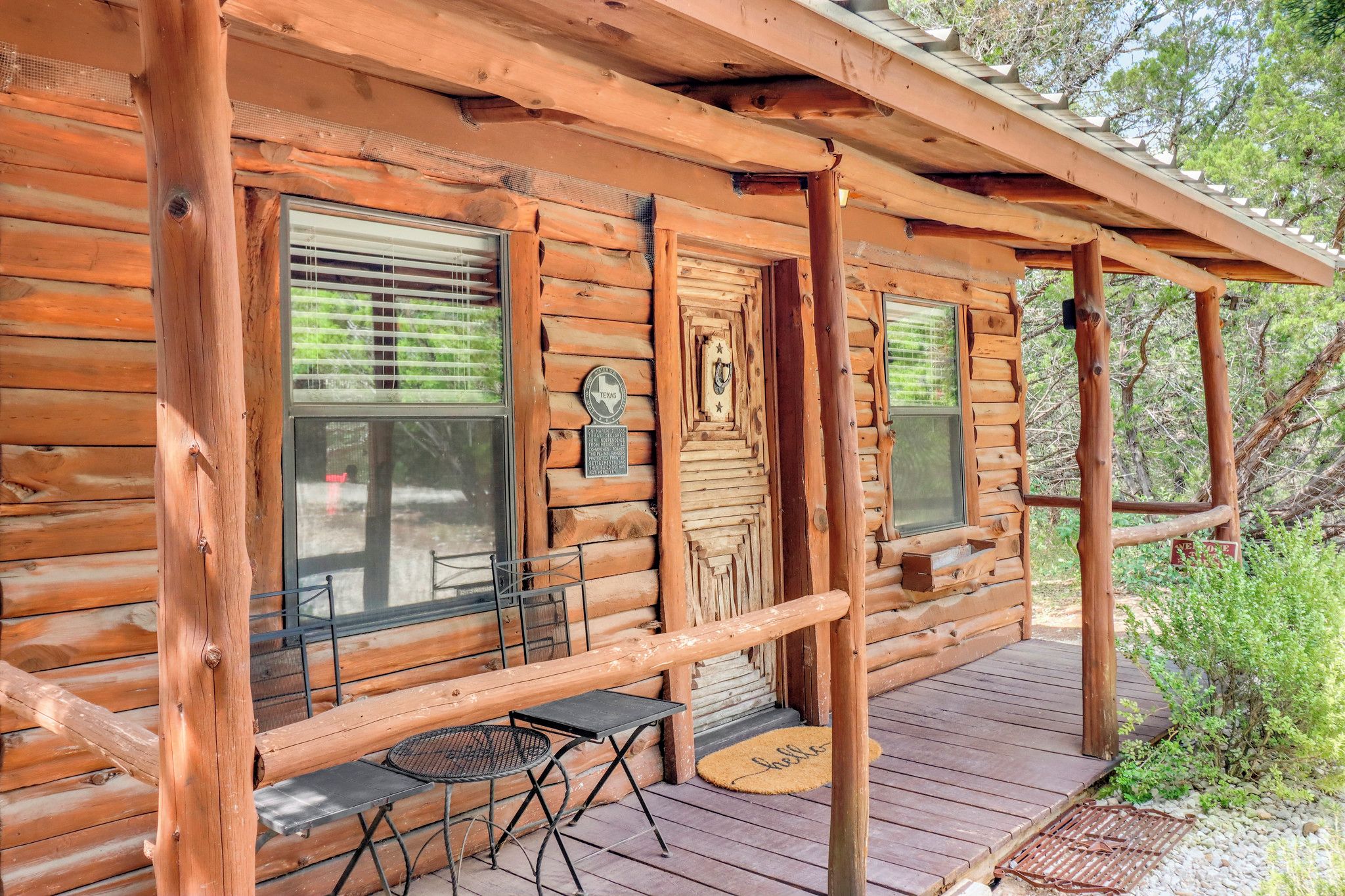 Une cabane en rondins avec un porche, une table avec des chaises et une porte ornée d’une enseigne indiquant « Texas ».