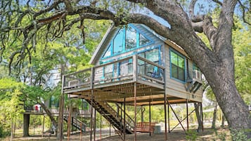 Uma casa na árvore com deck de madeira, escada e guarda-corpo de metal.