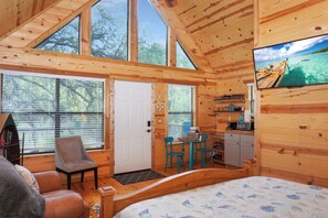 Une cabane en bois avec un lit, un bureau, une chaise et un téléviseur.