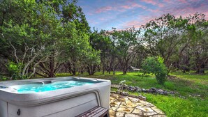 A hot tub with a wooden bench in a garden with stone flooring and trees. - Canyon Vista I Romantic, hot tub, log cabin (Wimberley)