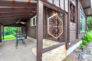 A wooden house with a covered patio, stone steps, and a decorative metal gate. - Canyon Vista I Romantic, hot tub, log cabin (Wimberley)