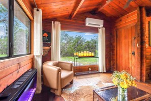 A log cabin interior with a leather chair, a piano, a fireplace, and a view of the outdoors. - Canyon Vista I Romantic, hot tub, log cabin (Wimberley)