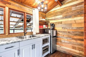 A kitchen with a sink, countertop, cabinets, a refrigerator, and a coffee maker. - Canyon Vista I Romantic, hot tub, log cabin (Wimberley)