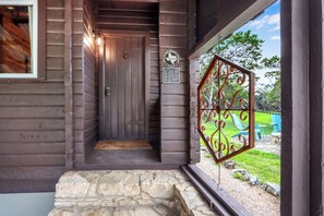 A wooden entrance with a stone step, a metal decorative gate, and a sign with historical text. - Canyon Vista I Romantic, hot tub, log cabin (Wimberley)