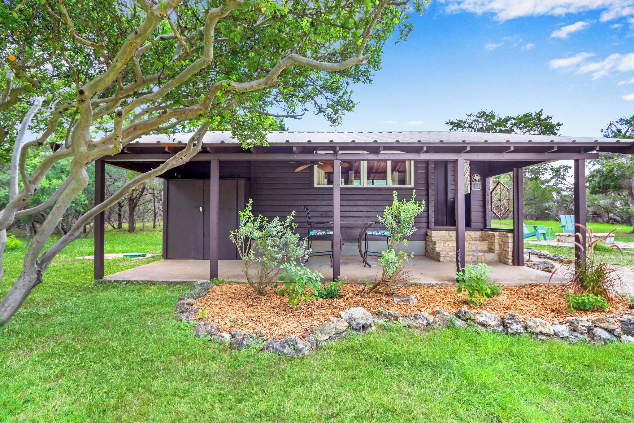 A wooden cabin with a covered patio, a stone fireplace, and a small garden area.