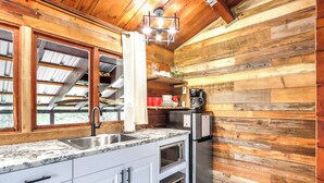 A kitchen with wooden walls, a granite countertop, a stainless steel sink, a coffee maker, and a built-in oven. - Canyon Vista I Romantic, hot tub, log cabin (Wimberley)