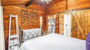 A wooden cabin bedroom with a bed, a metal railing, a wall-mounted bell system, and a large wooden door. - Canyon Vista I Romantic, hot tub, log cabin (Wimberley)