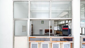 Una stanza con un'ampia finestra, un armadietto in legno e un oggetto rosso e nero sul davanzale.