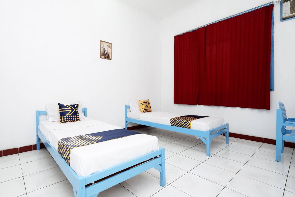 Quarto com duas camas azuis, roupa de cama branca e cortinas vermelhas.