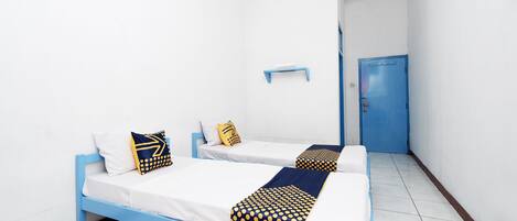 A room with two beds, each with white bedding and blue headboards. There is a blue door and a small shelf on the wall.