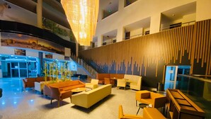 Eine großzügige Lobby mit modernem Design, ausgestattet mit einer zentralen Sitzecke mit Sofas und Sesseln, einer Treppe und einer dekorativen Hängeleuchte.