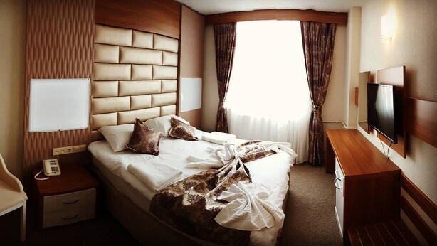 Ein Hotelzimmer mit einem großen Bett, einem Nachttisch mit Telefon, einem Fernseher und einem Holznachttisch.