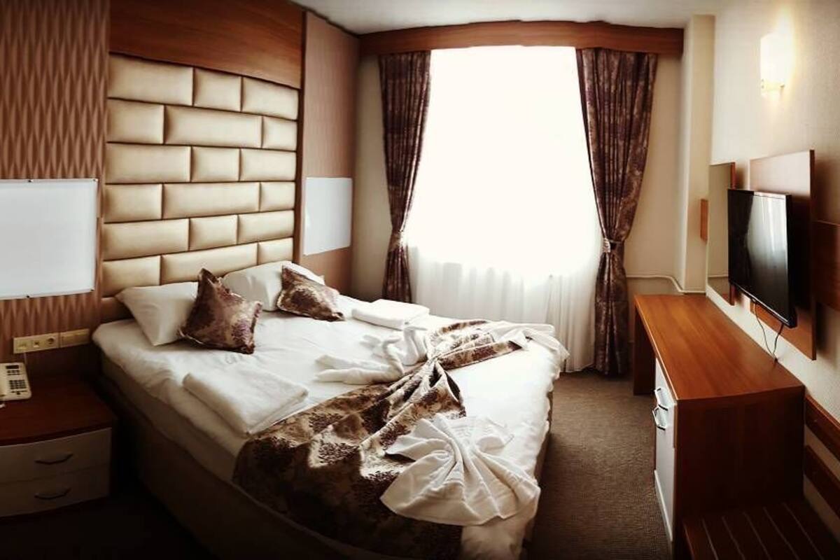 Ein Hotelzimmer mit einem großen Bett, einem Nachttisch mit Telefon, einem Fernseher und einem Holznachttisch.