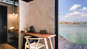 A wooden desk with a chair, a hanging light fixture, and a view of a calm body of water with hills in the distance. - Z9 Resort (Si Sawat)