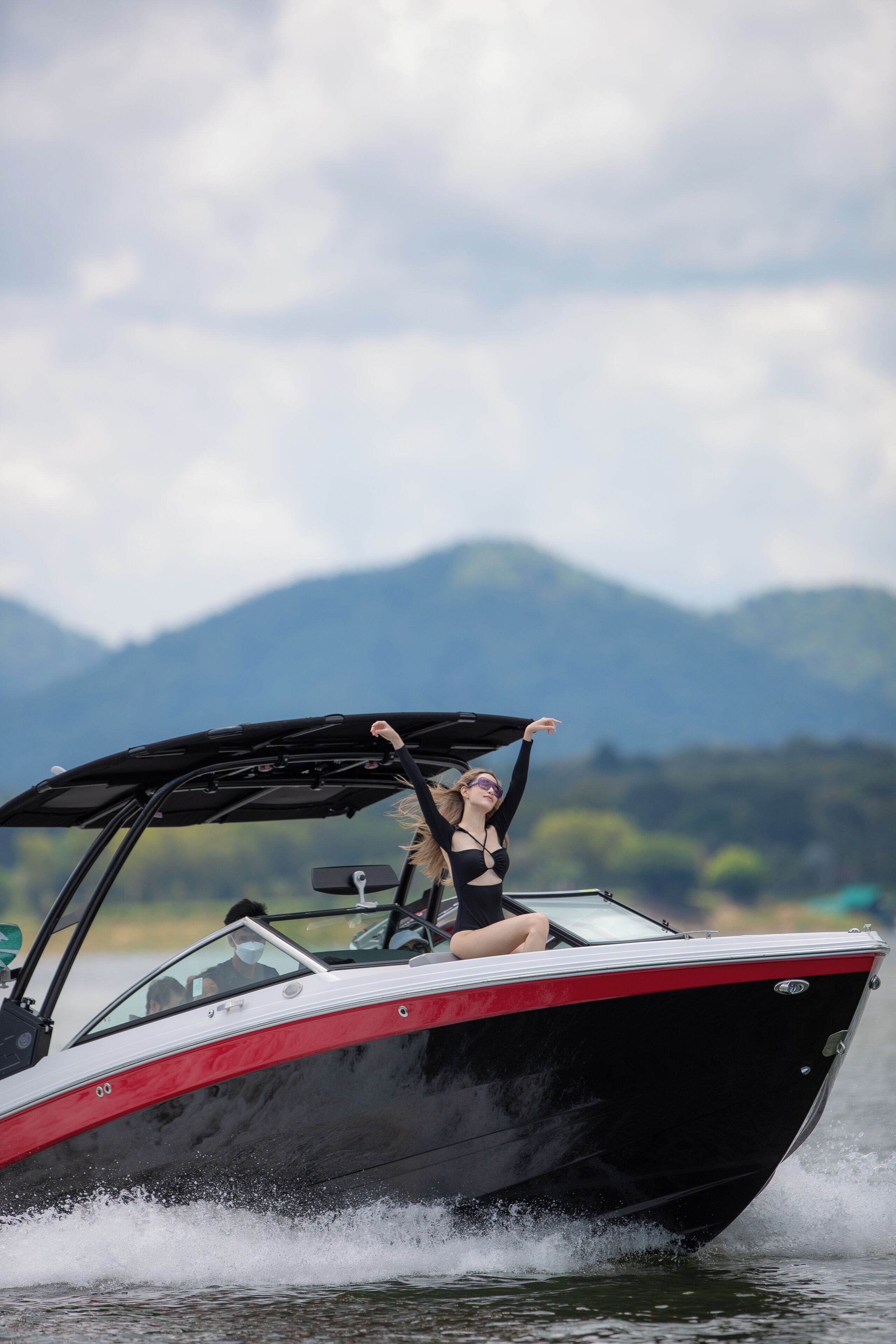 A speedboat with a person on the deck, water splashing around, and mountains in the background.
