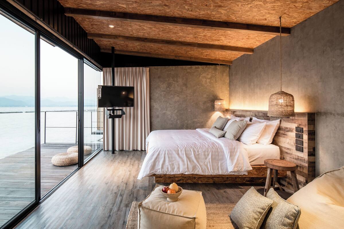 A modern bedroom with a large bed, a TV, and a view of the water.