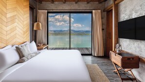 A bedroom with a large bed, wooden headboard, and a view of a lake and mountains. - Z9 Resort (Si Sawat)