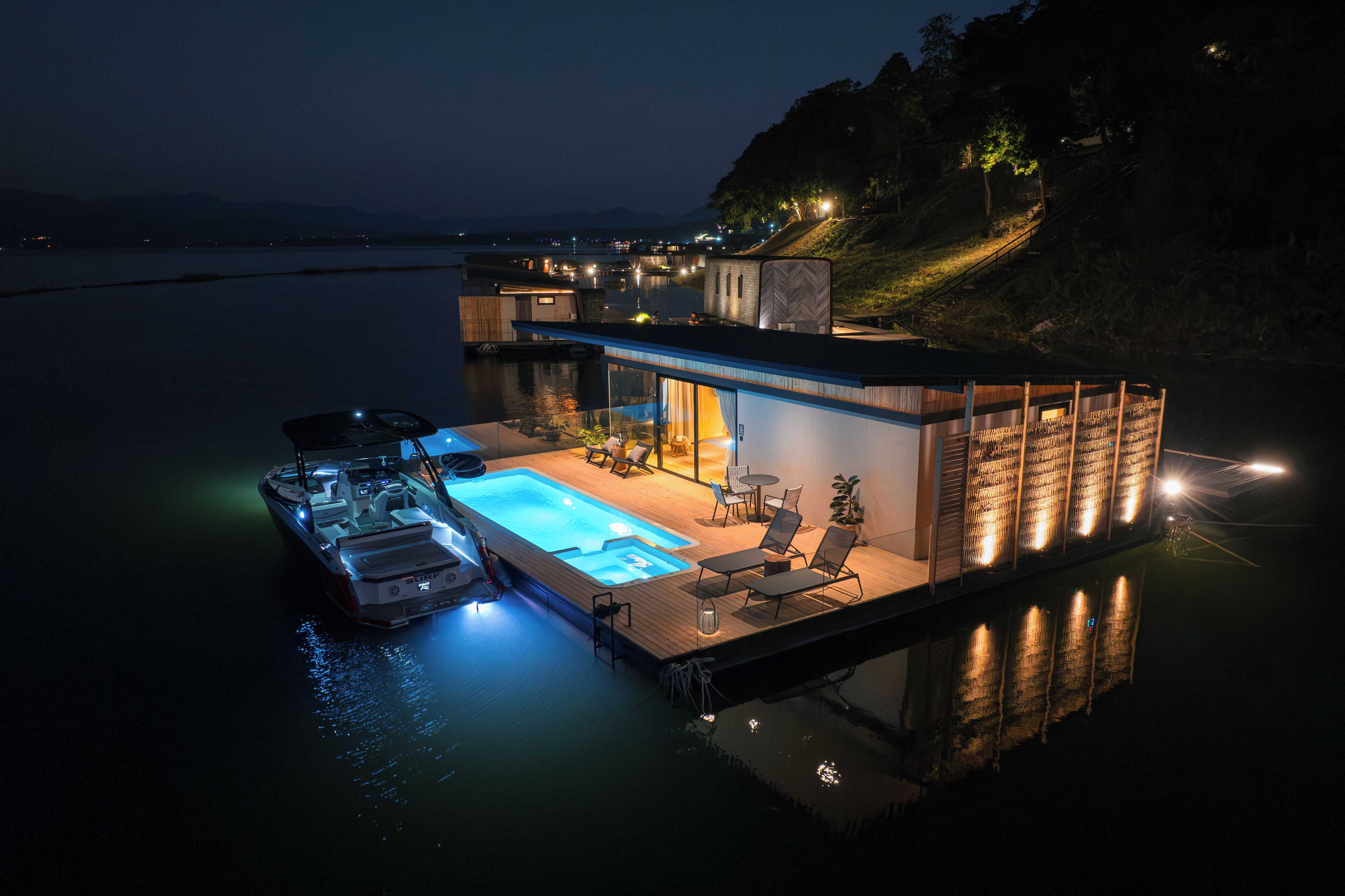 Una casa flotante con piscina, sillas de descanso y un bote.