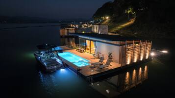 Una casa flotante con piscina, sillas de descanso y un bote.