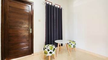 Quarto com porta de madeira, cortina escura e duas mesinhas com banquinhos estampados com folhas.