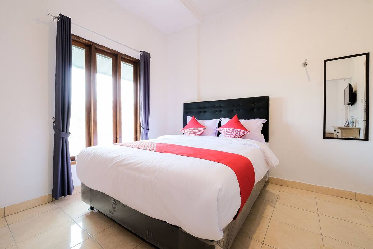 A neatly made bed with a white and red bedspread, a dark headboard, and a mirror on the wall.