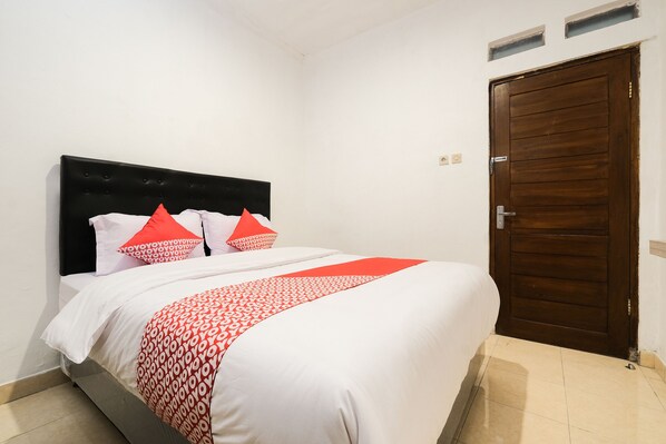 A neatly made bed with a white and red patterned bedspread, two red pillows, and a dark headboard in a room with a wooden door and white walls. - OYO 2118 Fh Stay (Depok)