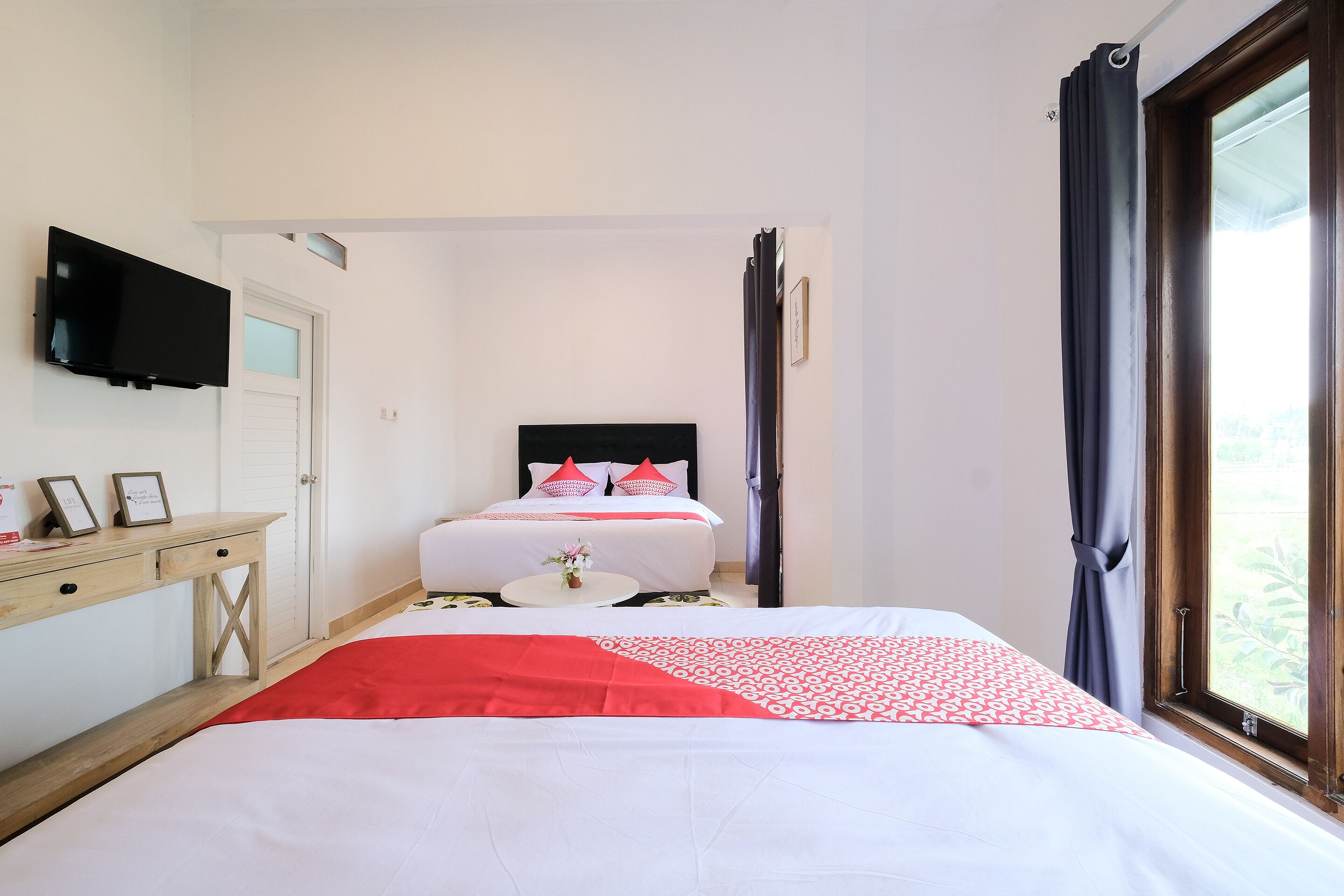 Quarto de hotel com cama, escrivaninha, televisão e janela com cortinas.
