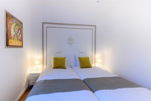 A double bed with white and gray bedding, two nightstands with lamps, and a framed picture on the wall. - Zythogite Appartement 9 personnes (Tintigny)